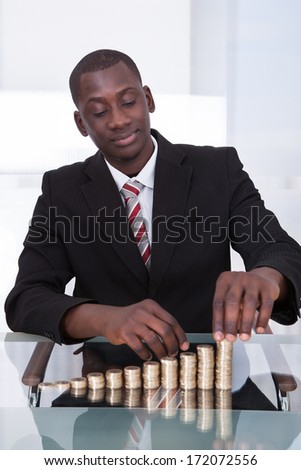 Portrait Of A Young African Businessman Stacking Coins On Desk