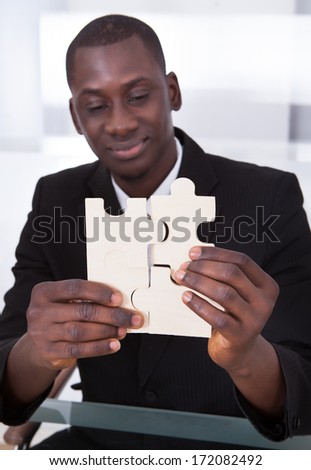Close-up Of A Happy African Businessman Holding Jigsaw Puzzle