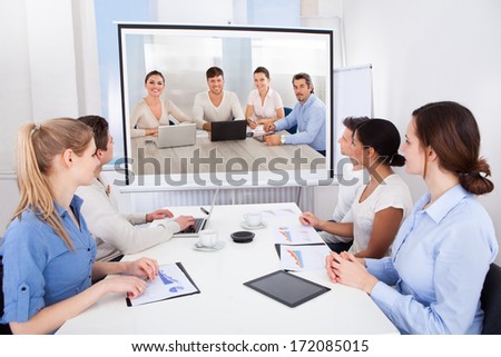 Businesspeople Sitting In Conference Room Looking At Projector Screen
