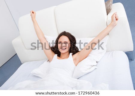 Portrait Of Young Woman With Hand Raised Lying On Bed