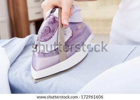 Close-up Of Woman\'s Hand Ironing Clothes On Ironing Board