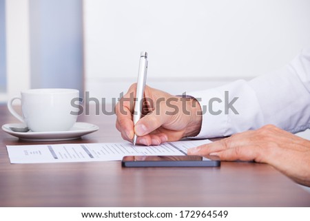 Close-up Of Businessman Writing On Paper With Pen