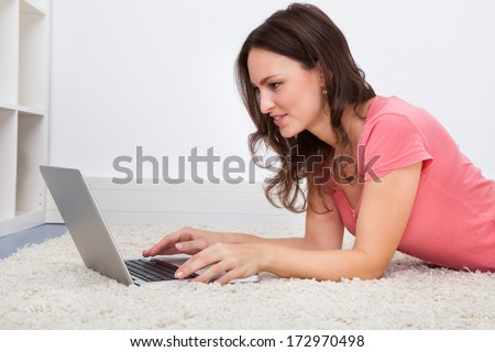 Portrait Of Smiling Young Woman Lying On Floor In Front Of Laptop