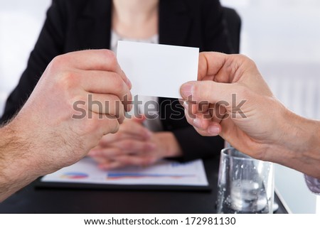 Businesspeople Exchanging Visiting Card In Front Of Colleague At Office Desk