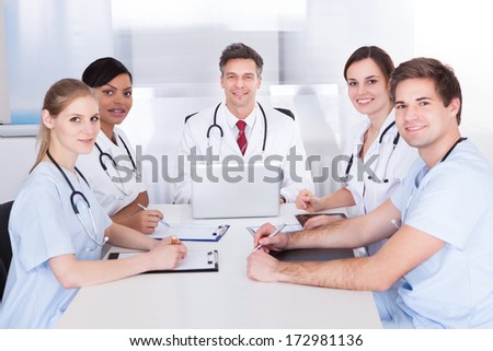 Happy Group Of Doctors Sitting In Meeting With Clipboard And Laptop