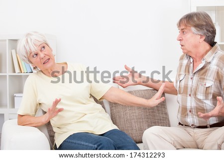 Portrait Of Senior Couple Sitting On Couch At Home Quarrelling With Each Other