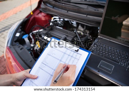 Male Mechanic Writing On Clipboard While Examining Car Engine