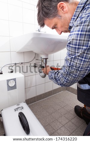 Mature Male Plumber Fitting Sink Pipe In Bathroom