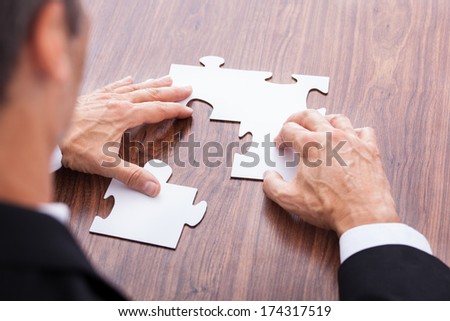 Portrait Of A Mature Businessman Solving Jigsaw Puzzle In Office