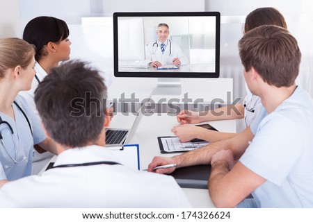 Group Of Doctors Looking At Online Presentation On Computer In Hospital