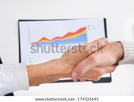 Two Businesspeople Shaking Hand In Front Of Graph