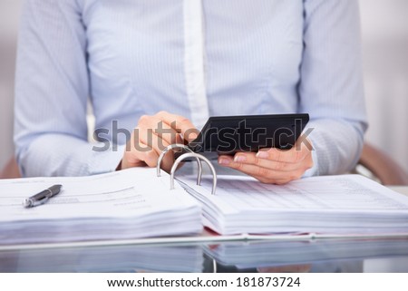 Close-up Of Businessperson Checking An Invoice On Calculator At Desk