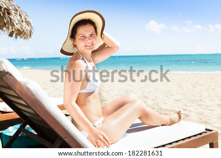 Portrait of attractive young woman in bikini relaxing on deck chair at beach