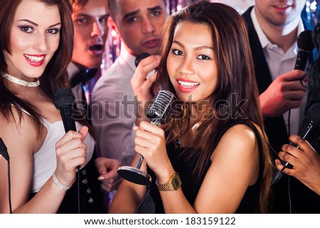 Portrait of beautiful women singing into microphones with male friends at karaoke party