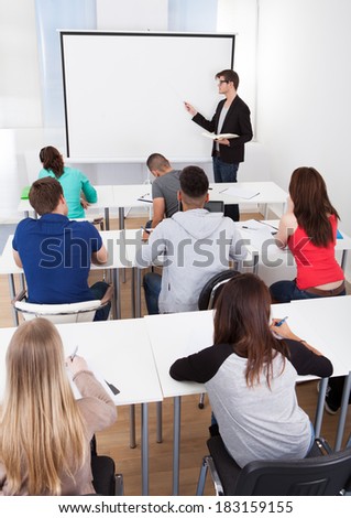 Young teacher teaching on whiteboard to college students in classroom