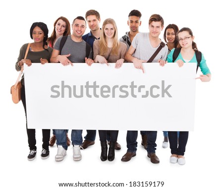 Full length portrait of confident multiethnic college students displaying blank billboard against white background