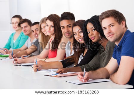 Portrait of multiethnic college students sitting in a row at desk
