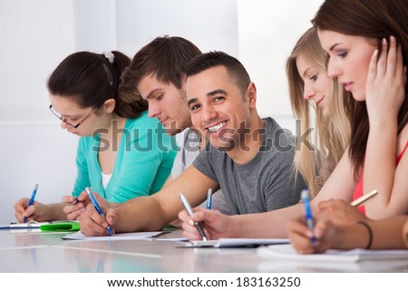Portrait of handsome university student sitting with classmates writing at desk