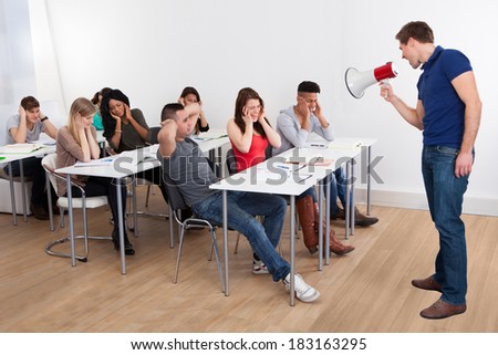 Angry teacher shouting through megaphone on university students in classroom