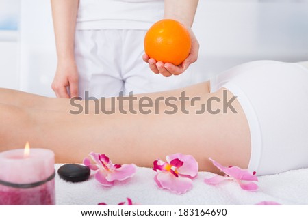 Female Massager Holding Orange Fruit In Front Of Woman Lying On Front