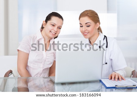 Portrait Of Young Female Doctor With Patient Looking At Laptop