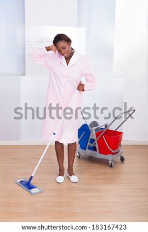 Full length of tired female housekeeper cleaning floor in hotel