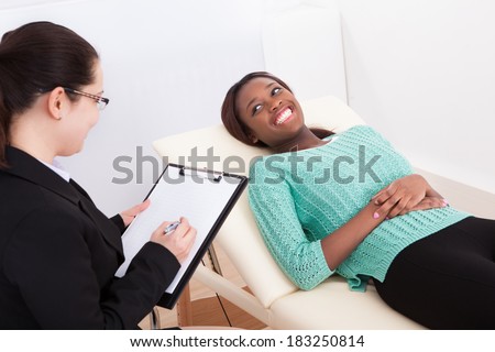 Happy female patient talking to psychologist while lying on bed in clinic