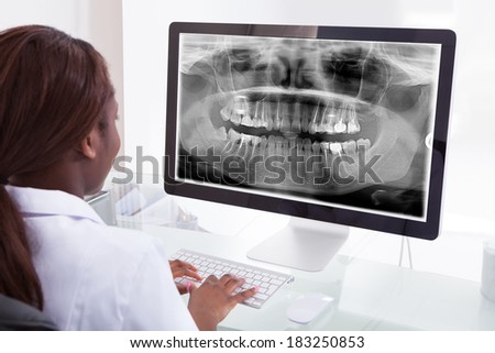 Rear view of female dentist examining jaw Xray on computer in clinic