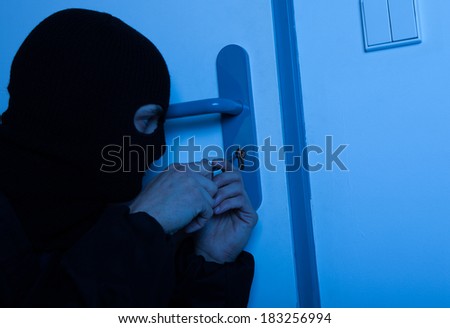 Thief in balaclava opening house door with tool