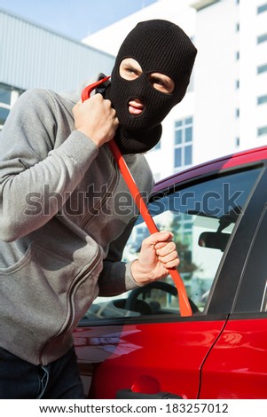 Thief in hooded jacket and balaclava opening car\'s door with crowbar