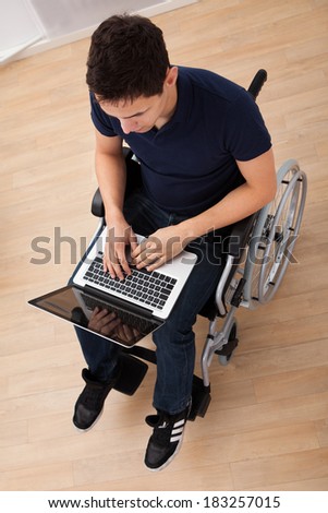 Full length of young handicapped man using laptop while sitting on wheelchair at home