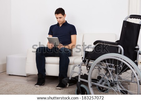 Full length of young handicapped man using digital tablet while sitting on sofa at home