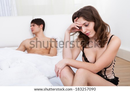 Sad young woman sitting with man on bed in background at home