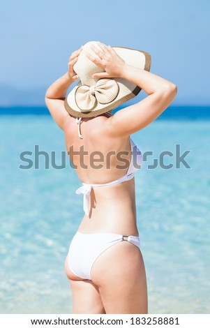 Rear view of young woman in bikini wearing sunhat at beach