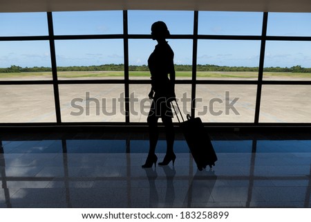 Silhouetted businesswoman with baggage walking against airport window