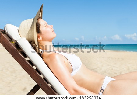 Side view of young woman in bikini sunbathing on deck chair at beach