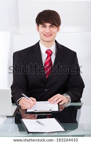 Portrait of confident businessman writing on paper at desk in office