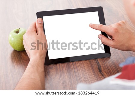 Cropped image of male college student using blank digital tablet by green apple on table