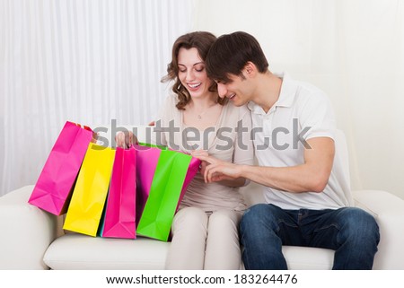 Portrait of young happy couple sitting on couch with shopping bags