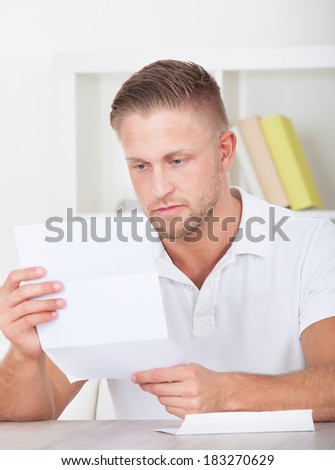 Man sitting reading a letter in an office with a serious expression with the envelope lying on the desk beside him
