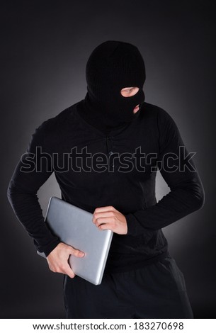 Thief stealing a laptop computer creeping furtively through the darkness as he makes his getaway  conceptual of data and identity theft
