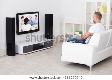 Man sitting on a sofa in his living room watching television alone at home