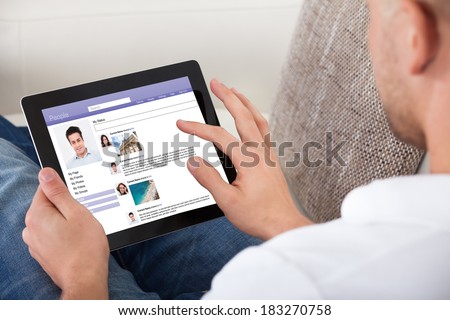 Man looking at personal profiles or comments left by viewers on a tablet computer navigating the touch screen with his finger over the shoulder view of the screen