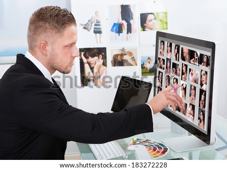 Businessman sitting at his desk in front of a large screen monitor editing photographs