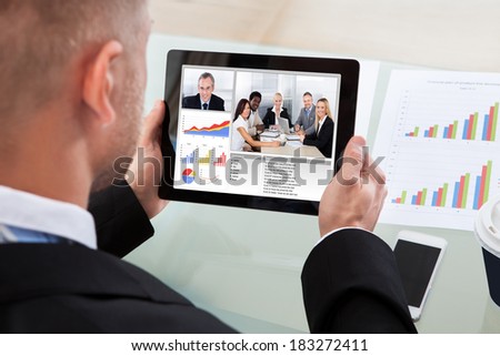 Businessman on a video or conference call on his tablet with an image of work colleagues in a meeting and bar graphs on the screen