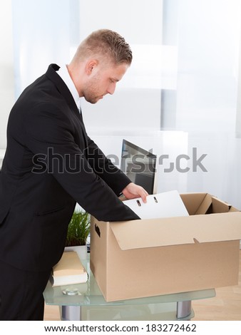 Businessman moving offices packing up all his personal belongings and files into a brown cardboard box