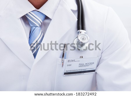 Close up of the pocket on a lab coat with a doctors ID tag and pen and the disc of his stethoscope hanging around his neck