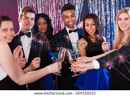 Happy multiethnic friends holding sparkling sticks while toasting drinks at nightclub