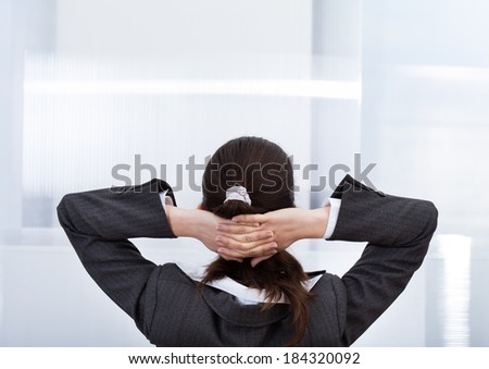 Rear view of businesswoman with hands behind head relaxing in office