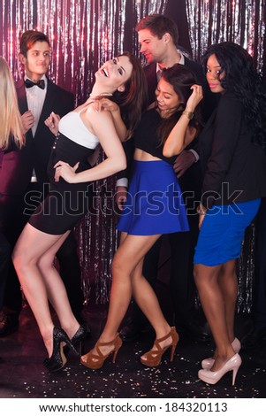 Full length portrait of happy women dancing with male friends in nightclub